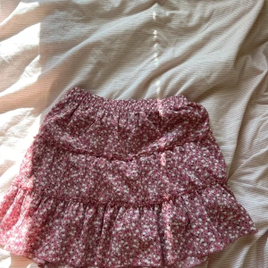 Blommig volangkjol från Zara - Supersöt kort kjol från Zara med rosa och vita blommor. Kjolen har volanger och ett smockat midjeband som gör den bekväm och lätt att bära. Perfekt för dig som gillar romantisk och feminin stil. Passar dig som är ca 13-14 år. I bra skick, har shorts under. 