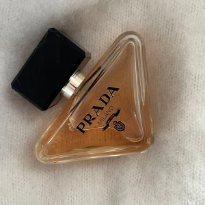 Prada Parfym Eau de Parfum 50ml - Exklusiv parfym från Prada i en unik trekantig glasflaska med svart, rektangulärt lock. Flaskan rymmer 50 ml Eau de Parfum och har en elegant beige-guldig vätska. Märket och loggan syns tydligt på framsidan. Perfekt för dig som gillar lyxiga dofter. Har använts vid få tillfällen! Nypris - 1200 på kicks. Färgen har bleknat lite men doften är den samma! Säljer då jag tycker att den doftar för mycket och är lite känslig!