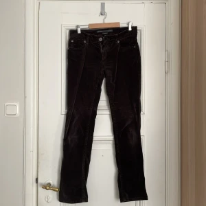 Bruna/svarta sammetsbyxor med rak passform - Marc opolo, Snygga bruna/svarta sammetsbyxor med klassisk femficksdesign och rak passform. Byxorna har knapp och dragkedja framtill samt bälteshällor. Perfekta för dig som gillar retrostil och vill ha ett mjukt material med cool struktur.