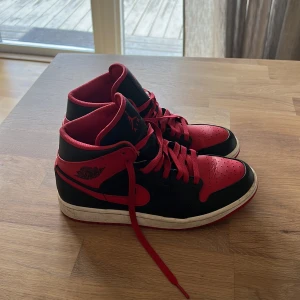 Nike Air Jordan 1 svart/röd US8 - Säljer ett par Nike Air Jordan 1 i klassisk svart och röd färg. Skorna har högt skaft, röd swoosh och snörning samt den ikoniska Jordan-loggan på sidan. Ovandelen är i skinn och mesh för extra komfort. Perfekta för dig som gillar streetstyle.