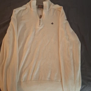 Beige merinoulltröja från Morris - Snygg beige långärmad tröja från Morris i 100% merinoull. Tröjan har en half zip med läderdetalj och en liten broderad logga på bröstet. Perfekt för dig som gillar stilrena och klassiska plagg med skön passform. Står storlek M men passar mycket bättre som en size small