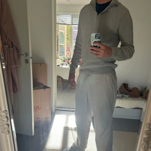 Grå ribbad half zip stickad tröja Dobbler - Säljer en stilren grå stickad tröja med ribbad struktur och half zip-dragkedja i halsen. Tröjan har lång ärm och en klassisk passform som funkar till många olika looks. Perfekt för dig som gillar en clean och enkel stil.