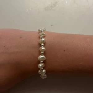 Pärlarmband med silverfärgade detaljer - Stilrent armband med oregelbundna vita pärlor och små silverfärgade kulor mellan varje pärla. Perfekt accessoar för att lyfta din outfit med en klassisk och fräsch touch. Handgjort 