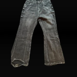 Svarta bootcut jeans med slitna benslut - Säljer ett par svarta bootcut jeans med snyggt slitna benslut och klassisk femficksdesign. Jeansen har en mörk tvätt med ljusa slitningar och breda ben.