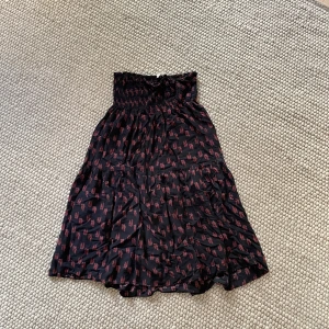 Smockad midikjol Mayla Stockholm - Blommig svart midikjol med smock i midjan 💕 köpt på NK för 1800kr, väldigt snygg passform! Dock är smocken i midjan skadad, därav det låga priset, se bild 3! Går att använda som vanligt trots skadan 🫶🏻