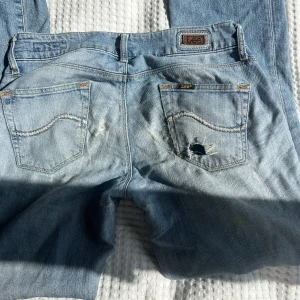 Ljusblå slitna jeans från Lee - Ljusblå jeans från Lee med tydliga slitningar och hål på bakficka och ben. Klassisk femficksmodell med Lee-logga på bakfickan. Jeansen har en avslappnad vibe och är tillverkade i bomullsdenim.