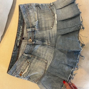 Jeanskjol med volang  - Superfin ljusblå jeanskjol från Esprit med volangkant och råa kanter. Klassisk femficksmodell med snygga detaljer och broderade bakfickor. Kjolen har en kort och trendig passform, perfekt för dig som gillar en edgy denimstil.