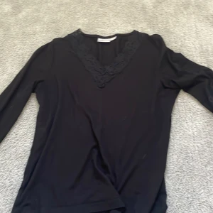 Svart långärmad topp med spets Gina Tricot - Svart långärmad topp från Gina Tricot med snygg v-ringning och dekorativ spetsdetalj runt halsen. Mjuk och skön, perfekt till jeans eller kjol. Enkel men ändå lite extra tack vare spetsen.