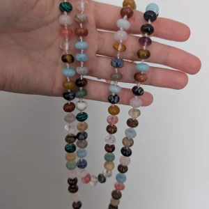 Färgglatt halsband med pärlor - Långt halsband med massor av färgglada pärlor i olika former och nyanser. Pärlorna är runda och platta, och kommer i färger som blå, grön, rosa, brun, svart, vit och gul. Perfekt för dig som vill ha en unik och lekfull accessoar som sticker ut.