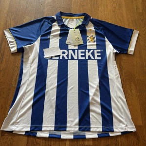 IFK Göteborg matchtröja - Säljer en officiell IFK Göteborg fotbollströja från Craft i blått och vitt med klubbmärke och sponsortryck. Tröjan har klassiska vertikala ränder, krage och korta ärmar. Perfekt för dig som vill visa ditt stöd på läktaren eller hemma.