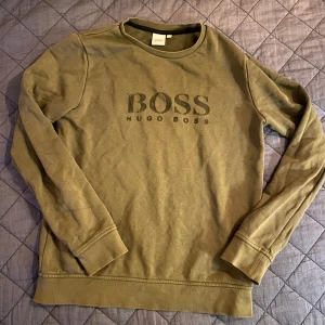 Olivgrön sweatshirt från Hugo Boss - Snygg olivgrön sweatshirt från Hugo Boss med stort BOSS-tryck på bröstet. Tröjan har rund halsringning, långa ärmar och är gjord i mjuk bomull. Perfekt för en chill och stilren look.