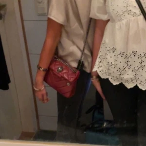 Röd väska från Kurt gieger kedja - Säljer en snygg röd axelväska med quiltat mönster och silverfärgad kedjerem. Väskan har ett vridlås framtill och en kompakt, boxig form som ger en trendig look. Perfekt för att lyfta vilken outfit som helst.