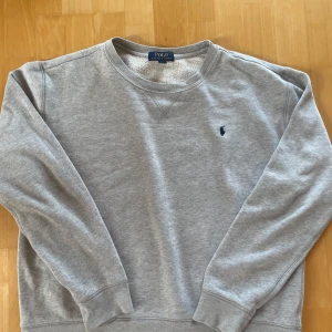 Grå sweatshirt från Polo Ralph Lauren XL - Klassisk grå sweatshirt från Polo Ralph Lauren i storlek S  Tröjan har rund hals, lång ärm och den ikoniska broderade loggan på bröstet. Mjuk insida och ribbade muddar för extra komfort. Perfekt för en chill och stilren look.