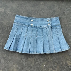 Ljusblå plisserad jeanskjol - Superfin ljusblå jeanskjol med plisserad design och dubbla silverknappar framtill. Kjolen är kort och har en klassisk denimlook som passar perfekt till sneakers eller boots. Snygg midja och coola detaljer gör den till ett måste i garderoben. Midja:41cm Längd:30cm. Lånade bilder!
