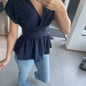 Mörkblå omlottopp från SHEIN - Snygg mörkblå omlottopp från SHEIN med bred midjedetalj och v-ringning. Toppen har korta ärmar och ett flowy fall nedtill som ger en feminin siluett. Perfekt att styla med jeans eller kjol för en trendig look.