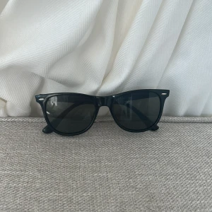 stilrena Svarta wayfarer solglasögon, perfekta till alla tillfällen  - Klassiska svarta wayfarer-inspirerade solglasögon med glansig båge och mörka glas. Snygg och tidlös modell som passar till allt. Snygga silvriga detaljer vid fronten. Perfekta för att lyfta din stil under soliga dagar.