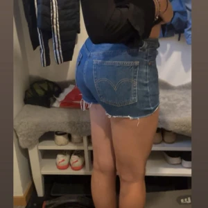 Blå jeansshorts från Levi's - Snygga blå jeansshorts från Levi's med klassiska bakfickor. Modellen är tight och midwaist, perfekt för sommardagar. Ikonisk Levi's-söm på bakfickorna och slitna detaljer för en avslappnad vibe. Finns även ett snöre som man får till. Pris kan diskuteras 