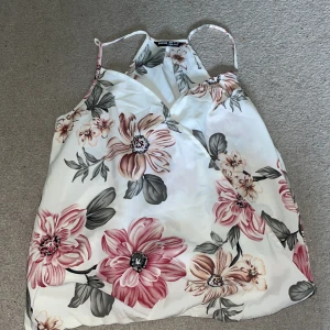 Blommig linnetopp  - Supersöt linnetopp från SHEIN med stora rosa och beige blommor på vit botten. Tunt och lätt material, smala axelband och snygg omlott-effekt framtill. 