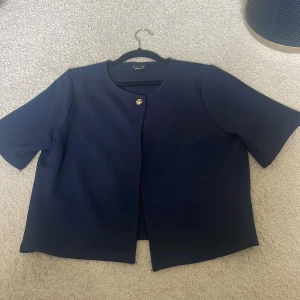 Mörkblå kofta med kort ärm - Stilren mörkblå kavaj från InWear med korta ärmar och rund halsringning. Jackan har en enkel knäppning med en dekorativ knapp framtill och rak passform. Perfekt för en clean och klassisk look.