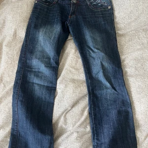 Blå Aragosta jeans med broderi - Snygga blå jeans från Aragosta med färgglada broderier och nitar på fickorna. Jeansen har kontrastsömmar i rött och gult, klassisk femficksmodell och raka ben. dem är köpta på second hand 💙