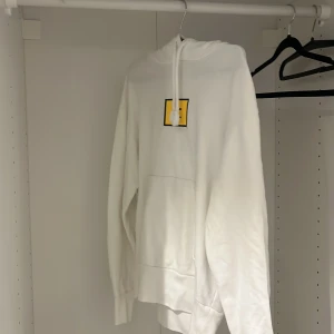 Vit hoodie Acne Studios - Vit hoodie från Acne Studios i bomull med Face-trycket i gult och svart på bröstet. Klassisk känguruficka, huva med snörning och långa ärmar. Perfekt när det börjar bli lite kallare. Ett litet hål i högerhörn vid loggan (sista bilden) pris är diskutabelt 