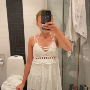 Vit spetsklänning med snörning - Superfin vit kortklänning i spets med smala axelband och snygg snörning framtill. Klänningen har v-ringning och detaljer i virkad spets, perfekt för sommarens alla tillfällen. Lätt och luftig modell med boho-vibbar.