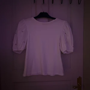 Vit blus med puffärm från Zara - Supersöt vit blus från Zara med puffiga korta ärmar och små pärldetaljer på ärmarna. Rund halsringning och rak passform. Perfekt för dig som vill ha en stilren men ändå unik topp med fina detaljer.