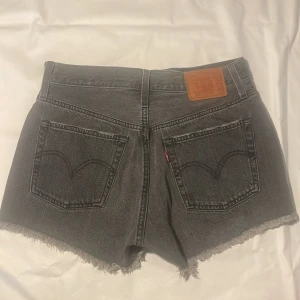 Grå Levi's jeansshorts med fransar - Snygga grå jeansshorts från Levi's med medelhög midja, slitna detaljer och fransig kant nedtill. Klassisk femficksmodell och Levi's läderpatch bak. 