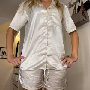 Silkesblanka vita pyjamasshorts - Snygga, glansiga pyjamasshorts i vit satin med elastisk midja och snörning. De är korta och har en avslappnad passform, perfekta för chill dagar eller mysiga nätter. Matchar toppen i samma material för en hel look. Säljer hela sättet så tröja och shorts. 