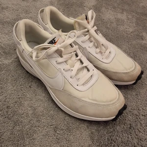 Vita Nike sneakers  - Snygga vita Nike sneakers med klassisk design, vita snören. Skorna har en bekväm platt sula. Perfekta för dig som gillar stilrena och fräscha sneakers.