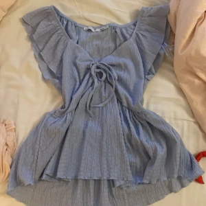 Ljusblå blus med volang - Supersöt ljusblå blus med volangärmar och v-ringning. Toppen har knyt framtill! Aldrig använd!