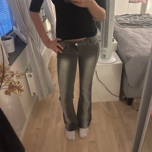 Svarta lågmidjade bootcut jeans med slitningar - Snygga svarta jeans med bootcut-modell och lätt slitna detaljer. Jeansen har klassisk femficksdesign, låg midja och är tillverkade i denim. Perfekta för dig som gillar en retro vibe och vill sticka ut lite extra.