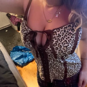 Leopardmönstrad korsett med snörning - Säljer en snygg leopardmönstrad korsett med bruna detaljer och snörning framtill. Toppen har smala axelband och markerade sömmar som ger en cool siluett. Perfekt för dig som vill sticka ut och addera lite edge till din outfit.