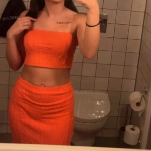 Orange figurnära kjol/ topp  - Säljer en snygg orange kjol med figurnära passform och enkel design. Kjolen är midjehög och har en slät yta utan mönster eller detaljer. Perfekt för dig som vill sticka ut med färg och gillar en stilren look.