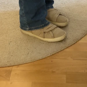 Beige skor med rosett från Dasia - Så söta slip-on sneakers från Dasia med en unik rosset/knytdetalj. De är i ganska bra skick men har lite tecken på användning tex lite fläckar. Om du undrar är de bara att skriva💕