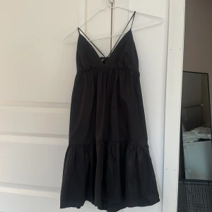 Svart kort klänning från Zara  - Supersöt svart kort klänning från Zara i storlek XS. Klänningen har tunna axelband, v-ringning och volang nertill. Snygg omlottkänsla i ryggen med knyt.  Knappt använt den så den är i jättebra skick. 