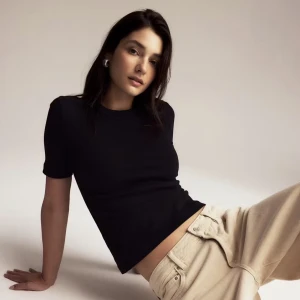 Svart ribbad t-shirt i bomull - En svart, ribbad t-shirt med korta ärmar och rund hals. T-shirten har en slim passform och är tillverkad i mjuk bomull, vilket gör den både bekväm och stilren. Perfekt att matcha med jeans eller kjol för en clean look. Den har dessa defekter som visas på bilden som jag tror jag tas bort i tvätten. Den har katt hår på sig. Den är 180 kr på gina så jag ger ett rätt så rättvist pris. Men vi kan diskutera pris!♡♡