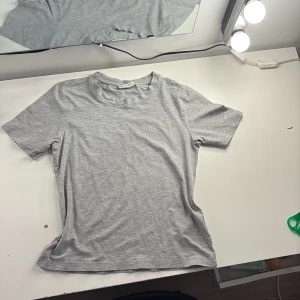 Ljusgrå basic t-shirt i bomull - Enkel och stilren ljusgrå t-shirt med rund hals och korta ärmar. T-shirten är i mjuk bomull och har en klassisk passform som funkar till allt. Perfekt för dig som gillar en clean och avslappnad look.