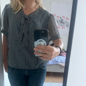Randig svartvit blus med knyt - Säljer en svart och vit randig blus med korta, transparenta ärmar och snygg knytning vid halsen. Blusen har en loose passform och tunna ränder som ger en cool look. Om ni har frågor är det bara att skriva💕💕