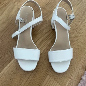 Klackskor med blockklack från Graceland storlek 37 - Stilrena vita sandaler från Graceland med bred rem över tårna och justerbart spänne vid ankeln. Skorna har en stabil blockklack och öppen tå, perfekta för en fräsch och modern look. Tillverkade i syntetmaterial med en klassisk design. Storlek 37, 7 cm höga 