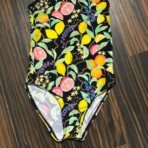 Färgglad baddräkt från Name It - Superfin baddräkt från Name It med tropiskt fruktmönster i gult, rosa, grönt och blått mot svart botten. Snygg detalj med diamantformat hål i ryggen och tunna axelband. Perfekt för poolen eller stranden i sommar! 