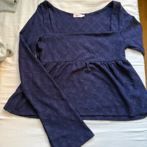 Mörkblå blus från Nelly - Supersöt mörkblå blus från Nelly med lång ärm och lätt struktur i tyget. Blusen har en markerad söm under bysten och lätt utställd nederdel. Perfekt för dig som gillar en feminin och trendig look. 