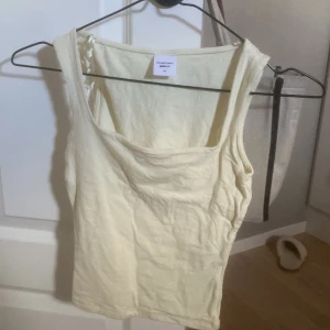 Ljusgul linnetopp från Gina - Säljer en ljusgul linnetopp från Weekday med breda axelband och enkel, stilren design. Toppen är ärmlös och gjord i mjuk bomull, perfekt för varma dagar eller att styla i lager. Superskön och lätt att matcha med jeans eller kjol.