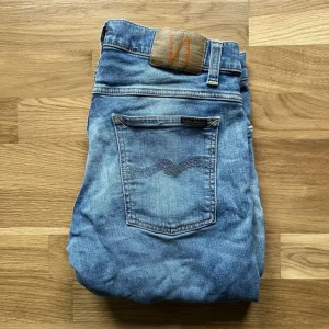 Ljusblå slim jeans från Nudie - Säljer ett par ljusblå slim jeans från Nudie Jeans som är ganska små i storlek som ungefär 32/34, dom har klassisk femficksdesign och snygga slitningar. Jeansen har en smal passform och är tillverkade i mjukt denimtyg av bomull. Perfekta för dig som gillar en clean och avslappnad look. 