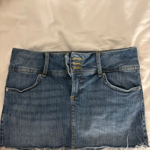 Jeanskjol med rå kant från Bershka - Snygg blå jeanskjol från Bershka i kort modell med rå, fransig nederkant. Klassisk femficksdesign, bälteshällor och gul kontrastsöm💗