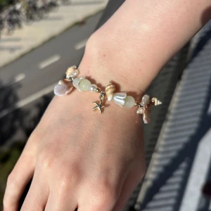Armband med snäckor och stjärnformad charm - Superfint armband med vita och beige pärlor, snäckor och en liten stjärnformad guldcharm. Armbandet har havsinspirerade detaljer och mix av pärlemor och guldtoner. Perfekt accessoar för en somrig vibe och strandkänsla.