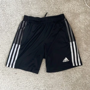 Svarta Adidas shorts med vita ränder - Säljer ett par bra och sparsamt använda träningsshorts från Adidas. Perfekta för sport och träning!