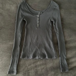 Blå/grå ribbad långärmad topp Pieces - Snygg blå/grå ribbad långärmad topp från Pieces i storlek S. Tajt passform men väldigt stretchig, med urringning och en knappdetalj. Endast använd ca 5 gånger och är i bra skick! 💗