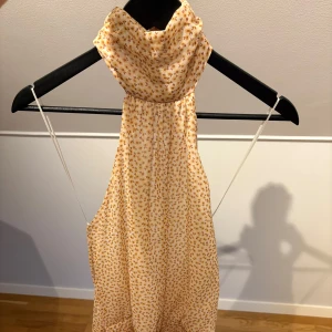 Ljusblommig halterneck sommarklänning - Supersöt ljus kortklänning med små blommor i beige och brunt. Halterneck med draperad krage och volang nertill. Tunn och luftig, perfekt för varma dagar. Sitter snyggt med öppen rygg🥰