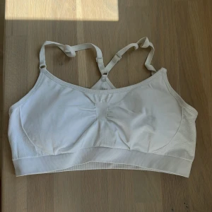 Vit sportig linnetopp från H&M - Säljer en vit sportig linnetopp från H&M med justerbara axelband och ribbad kant nedtill. Toppen har en enkel och clean design med lätt rynk framtill för extra passform. Perfekt för träning eller chill dagar.